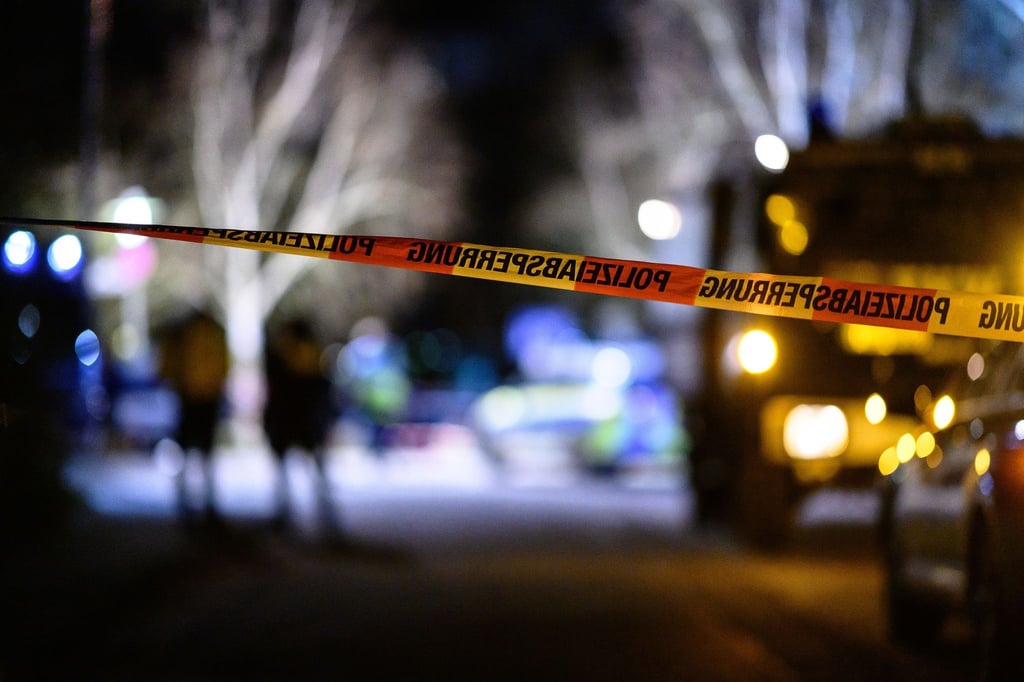 Ein Flatterband der Polizei ist vor Einsatzfahrzeugen am Tatort zu sehen.