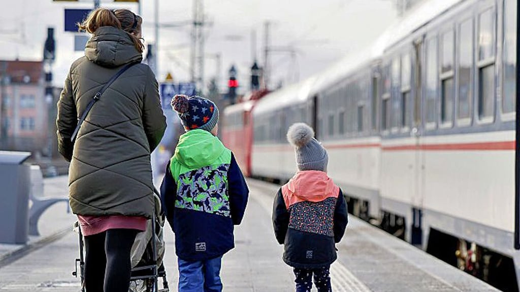 Eine Mutter mit ihren Kindern im Winter auf einem nicht überdachten Bahnsteig.