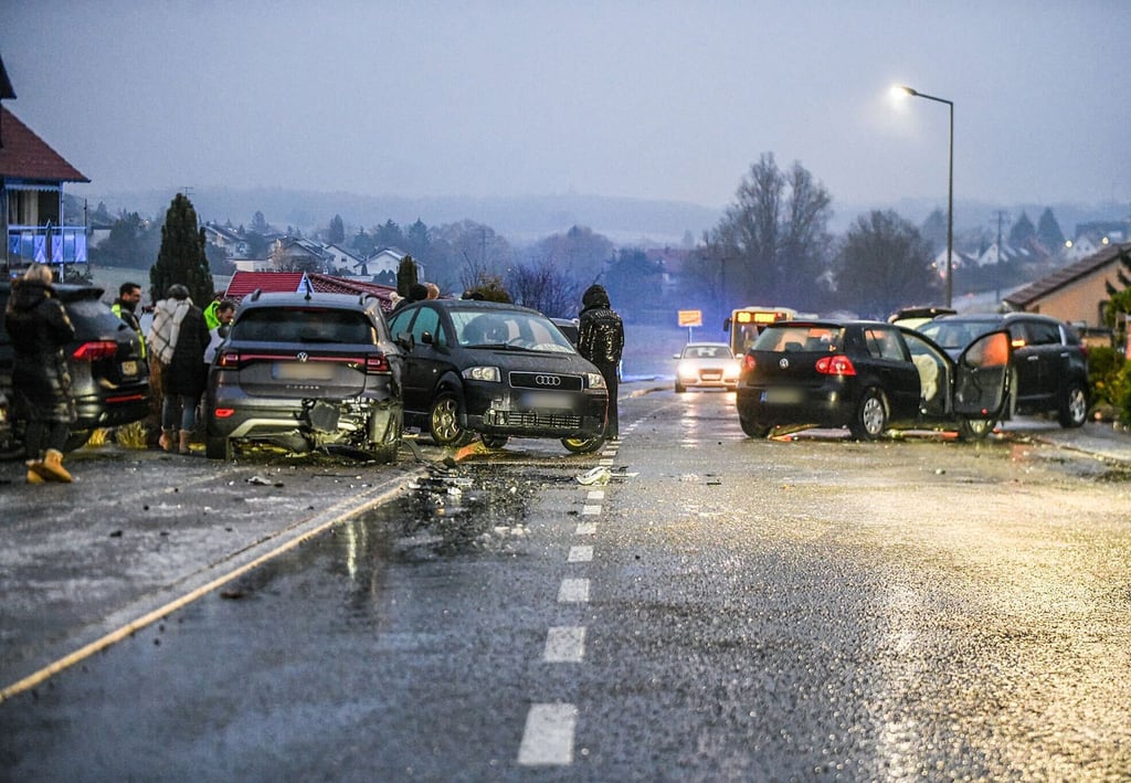 Nach einem Unfall bei Glatteis mit mehreren Fahrzeugen in Baden-Württemberg stehen Helfer und Beteiligte an den Autos auf einer Straße.