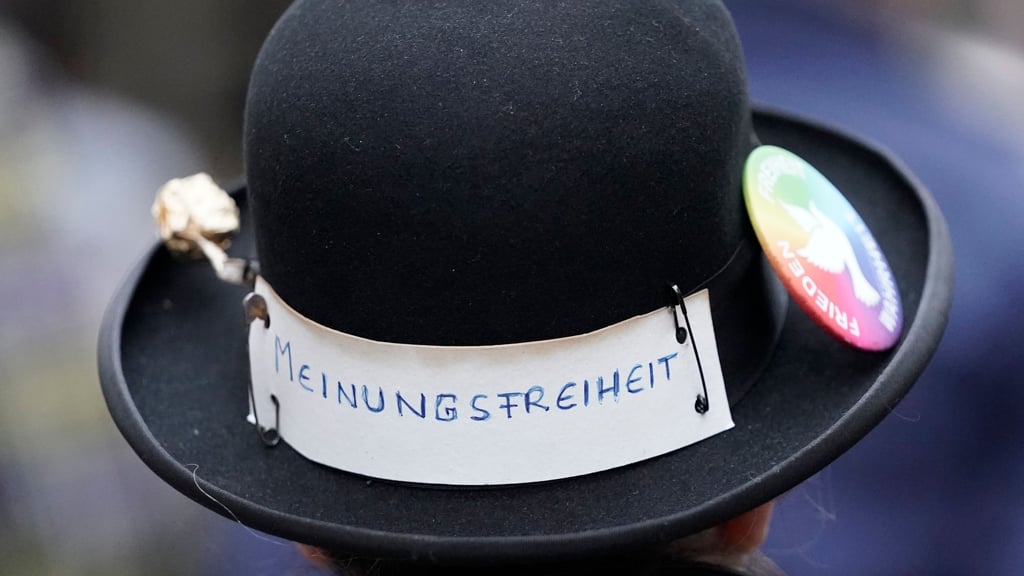 Eine Zuschauerin mit dem Aufkleber "Meinungsfreiheit" am Hut verfolgt eine Kundgebung.