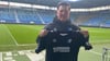 FCM-Trainer Christian Titz präsentiert das Sondertrikot, das seine Mannschaft im Heimspiel gegen Eintracht Braunschweig trafen wird.