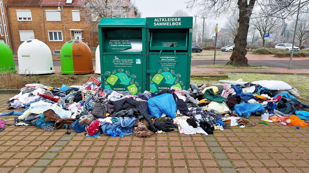 Textilien liegen verstreut um Altkleidercontainer am Nettomarkt in der Nähe des Salzwedels Bahnhofs herum.