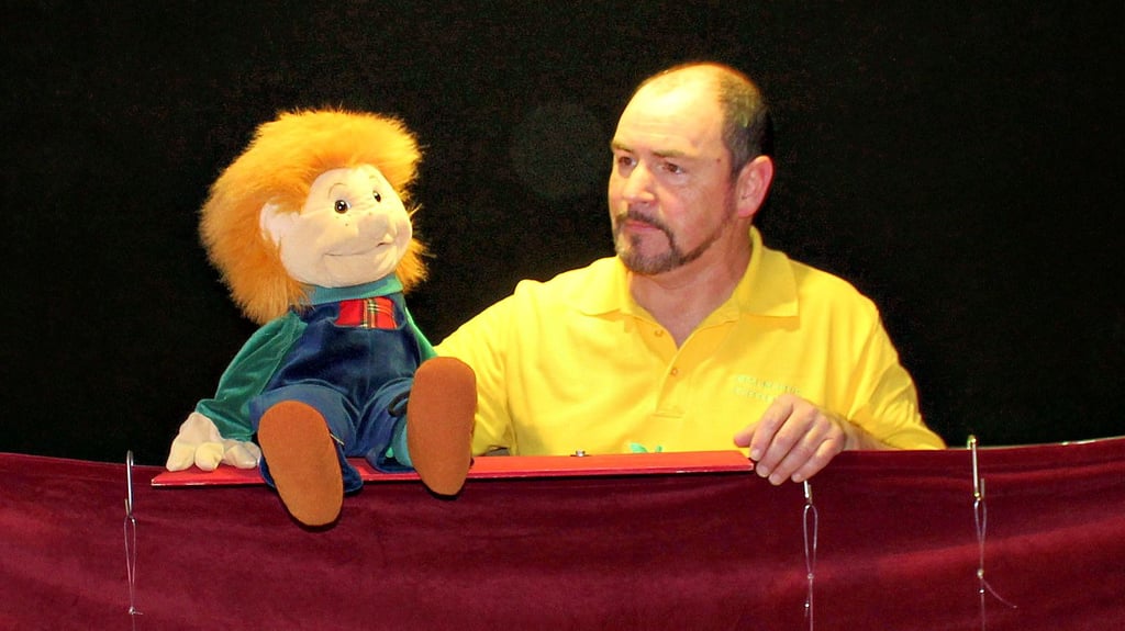 Rudolf Hein mit Puppe Tim bei der Bühnenprobe im Kindergarten Krümelkiste. Während einer Vorstellung sitzt er hinter einer Verkleidung aus Stoff unten an der Bühne.