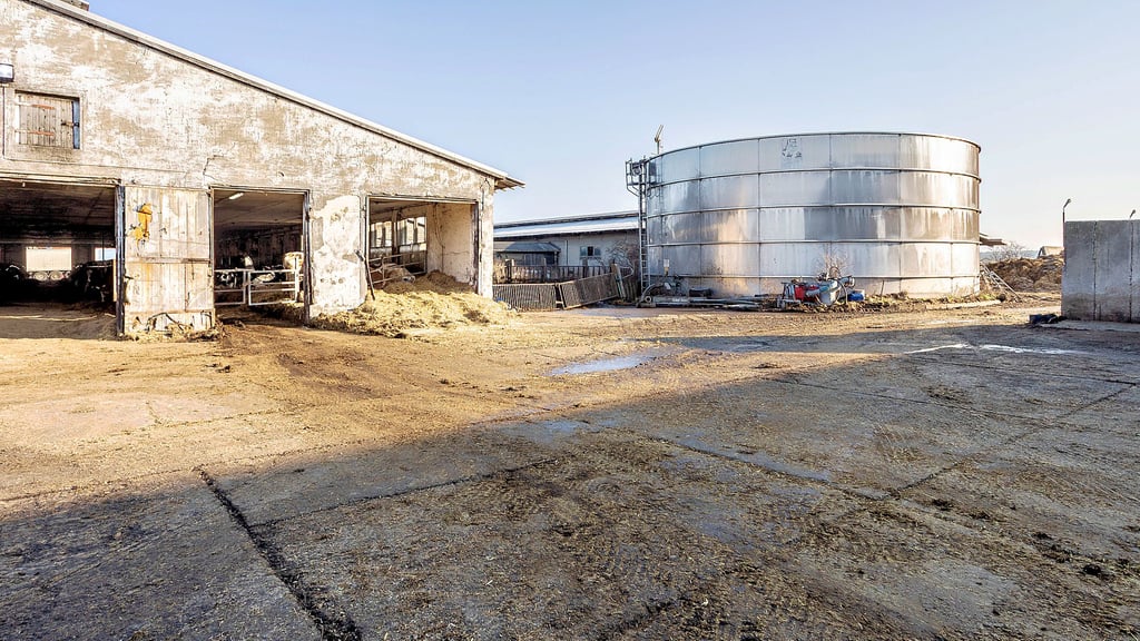 Über die Betonfläche vor dem Milchviehstall wird der Mist beim Reinigen geschoben. So erscheint die hier vorliegende Verschmutzung technisch bedingt und im üblichen Rahmen zu liegen. Über- oder ausgelaufene Gülle des silbern glänzenden Behälters ist nicht zu entdecken.