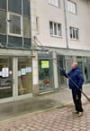 David Schulz  putzt mit einer Bürste an einer Teleskopstange die Glasfassade eines Treppenaufgangs in der Wallstraße in Köthen. 