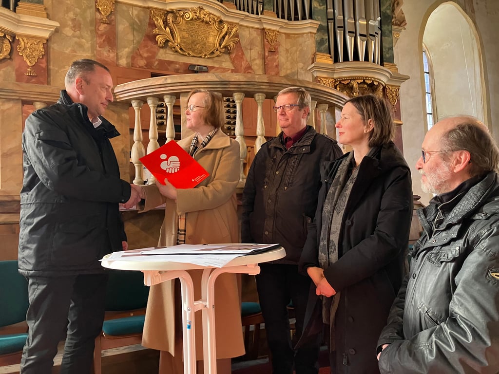 Vorstand Michael Näher überreicht die Fördermittel an Kirchenmusikdirektorin Martina Pohl. Bis 2026 soll eine neue Dauerausstellung auf der südlichen Empore zum Thema "Befreundete barocke Persönlichkeiten" entstehen.