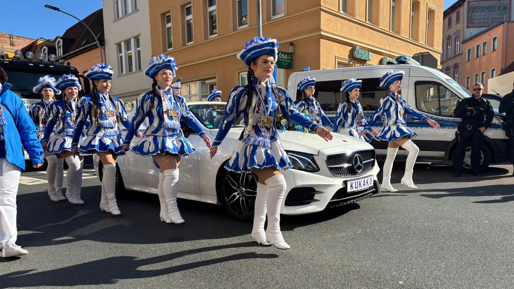 Die Prinzengarde des Kukakö marschiert neben einem weißen Cabriolet über die Weintraubenstraße in Köthen. Beamte der Landesbereitschaftspolizei (hinten) sichern den Umzug ab.