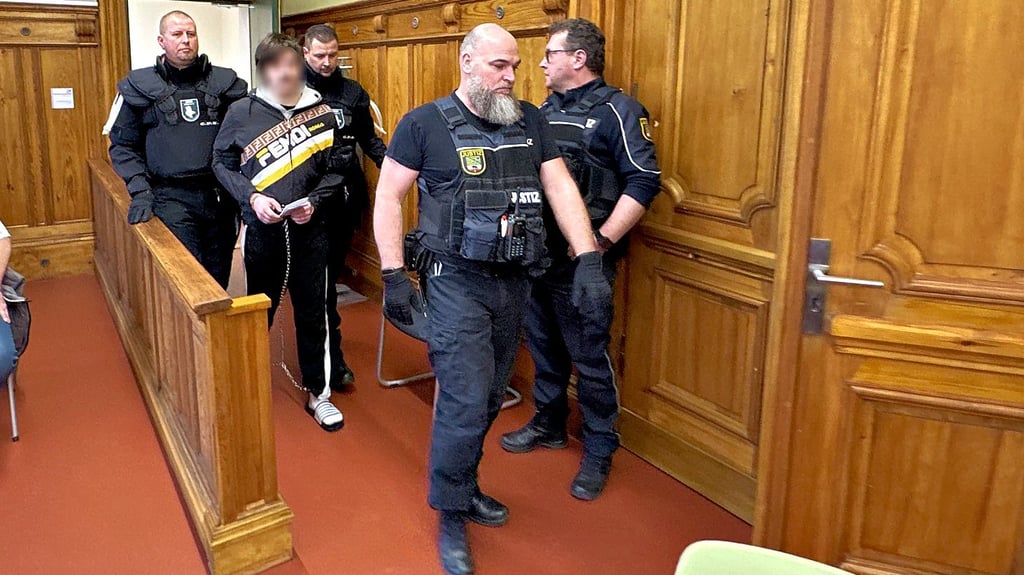 Justitzbeamte führen den Angeklagten mit Hand- und Fußfesseln in den Saal in Magdeburg.