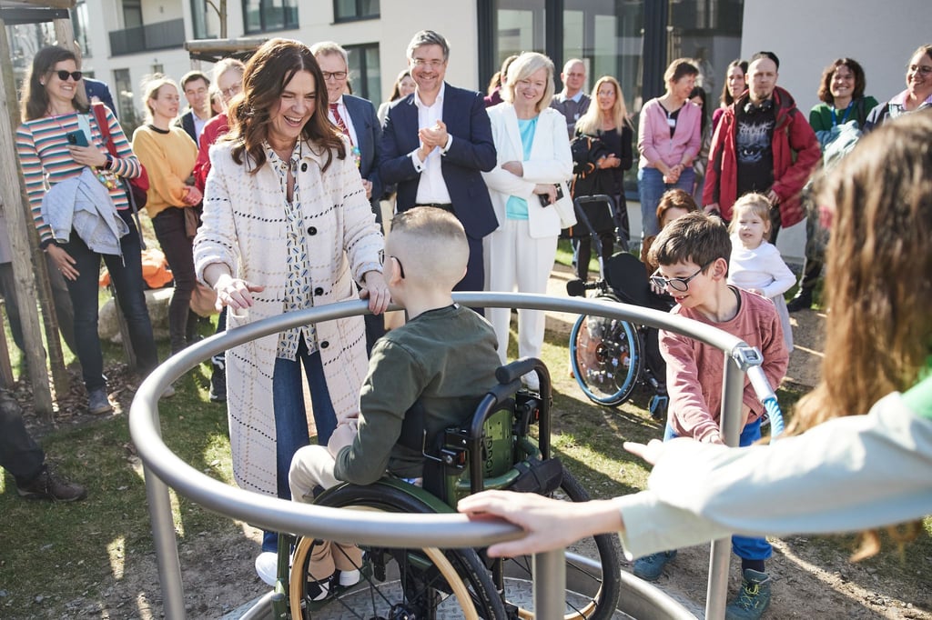 Ex-Eiskunstläuferin Katarina Witt gibt einem Jungen im Rollstuhl bei der feierlichen Eröffnung eines von ihrer Stiftung mitfinanzierten Spielplatzes Anschwung bei einem Karussell.