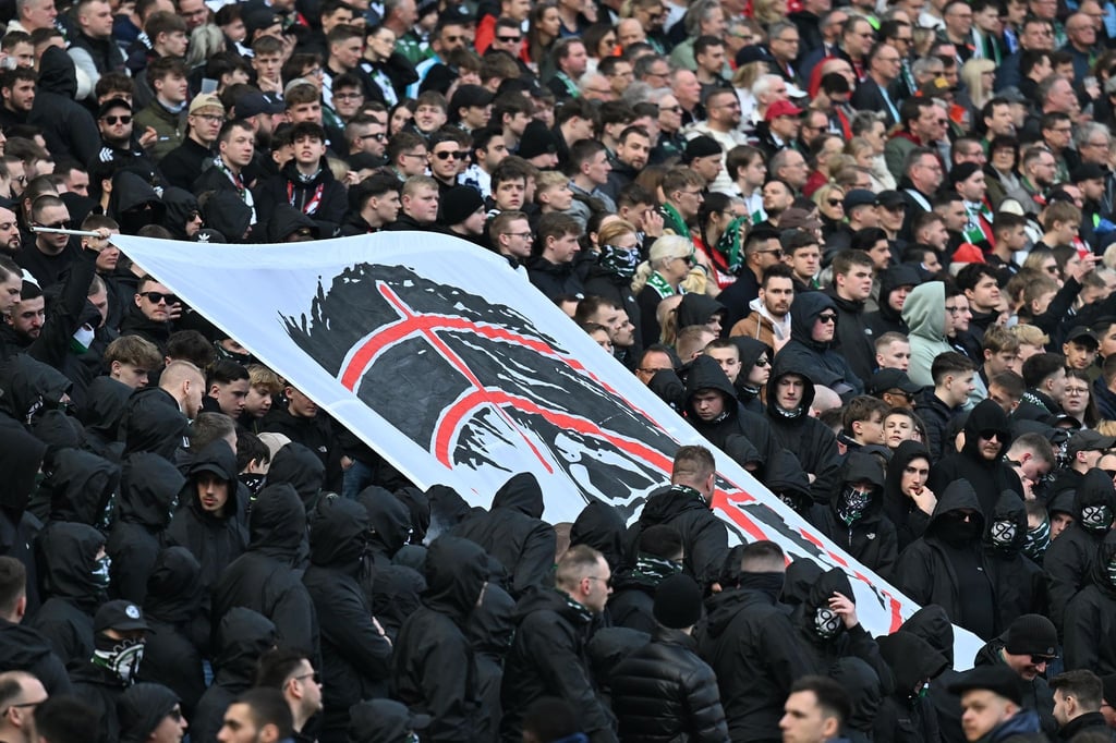 Hannover-Fans halten auf der Tribüne ein Plakat hoch, dass den Kopf von Niedersachsens Innenministerin Daniela Behrens in einem Fadenkreuz zeigt.