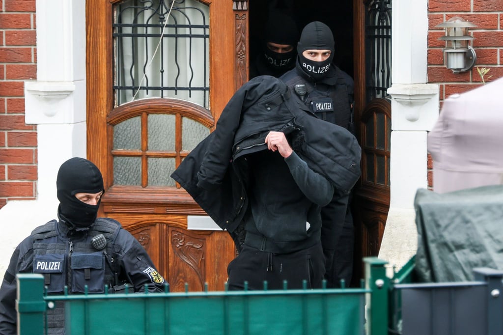 Polizeibeamte führen einen Tatverdächtigen aus einem durchsuchten Haus.