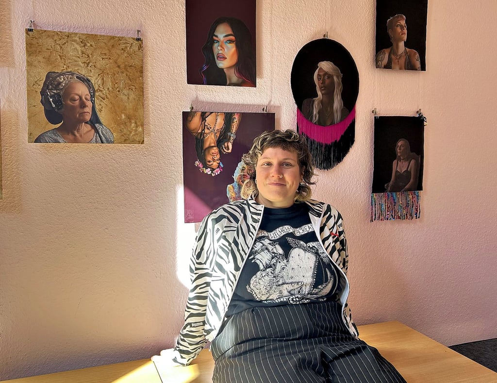 Sophie Lenglachner ist die Magdeburger Künstlerin der Ausstellung „Imagine Women“ im Volksbad Buckau. Hinter ihr an der Wand sind Bilder von Transfrauen zu sehen, die von der KI erstellt wurden.