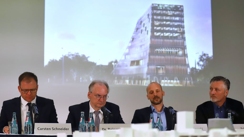 Der Ostbeauftragte Carsten Schneider, Sachsen-Anhalts Ministerpräsident Reiner Haseloff (CDU), Architekt Jan Musikowski und Landschaftsarchitekt Tobias Micke sitzen vor einem Entwurf des Zukunftszentrums in Halle.
