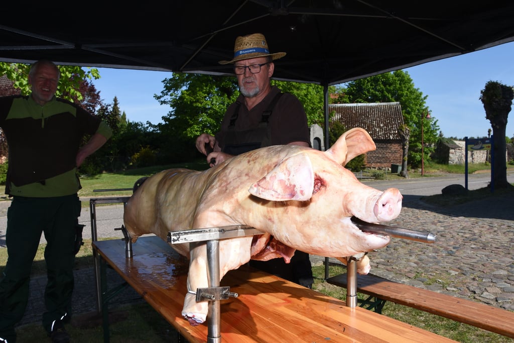 Holger Münz bereitet in Altmersleben ein Schwein am Spieß zu. Und nicht nur Feuerwehrmann Steffen Liermann (links) schaut dabei interessiert zu.