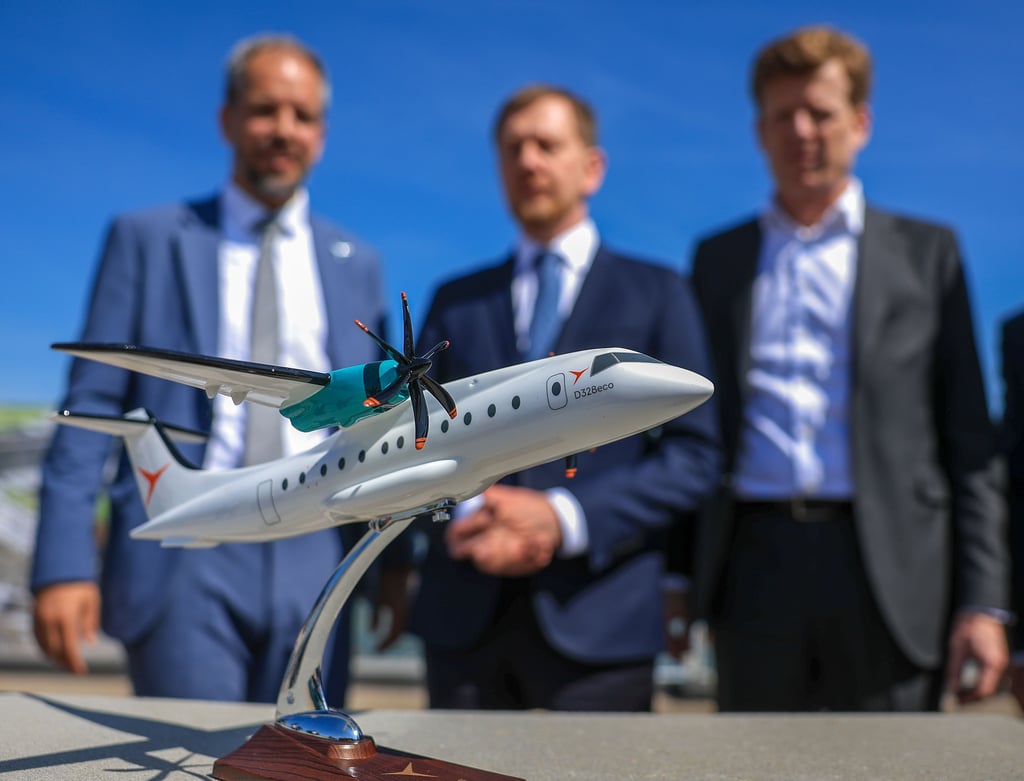 Nico Neumann (l-r), Co-CEO Deutsche Aircraft, Michael Kretschmer (CDU), Ministerpräsident von Sachsen, und Götz Ahmelmann, CEO der Mitteldeutsche Flughafen AG, stehen hinter dem Flugzeugmodell der D328 Eco nach der Grundsteinlegung für ein neues Flugzeugwerk auf dem Flughafen Leipzig/Halle.