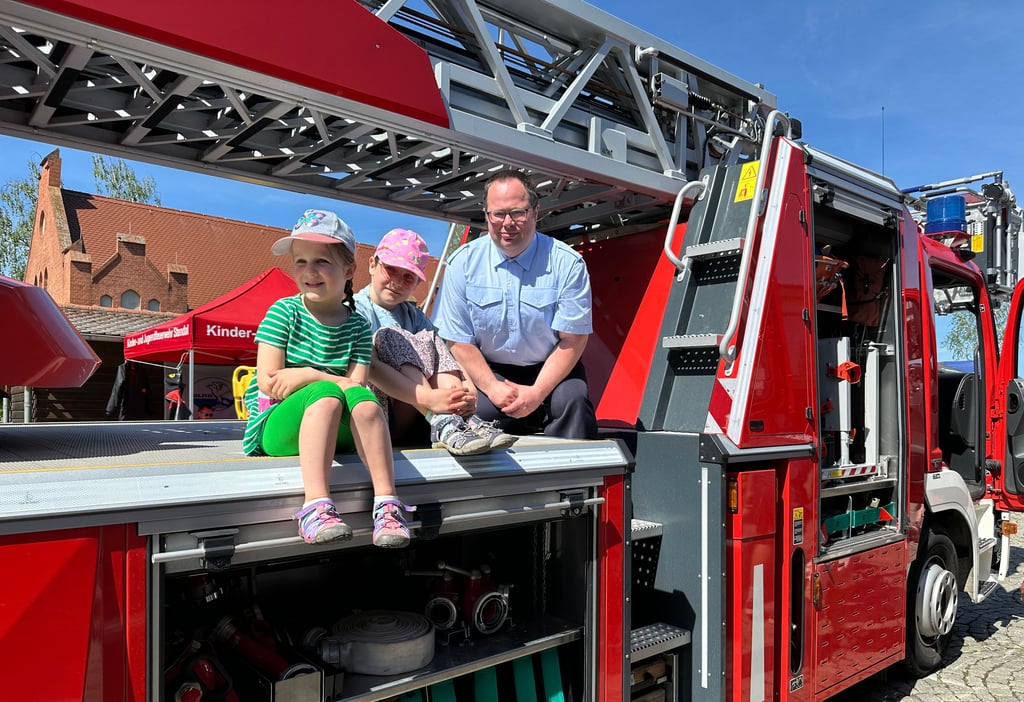 Martin Schulz (rechts) zeigt Alma (5) und Elsa (8) beim Tag der offenen Tür bei der Freiwilligen Feuerwehr Stendal am 1. Mai 2025 die Drehleiter.
