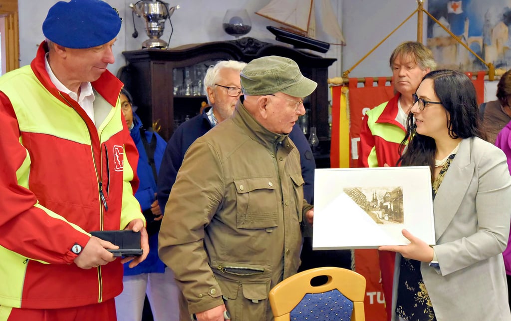 Im Beisein von Raymond Schulz (l.) überreicht Klaus Jurke (M.) vom Malzirkel Konsulin Courtney Mazzone (r.) eine Stadtansicht von Köthen.