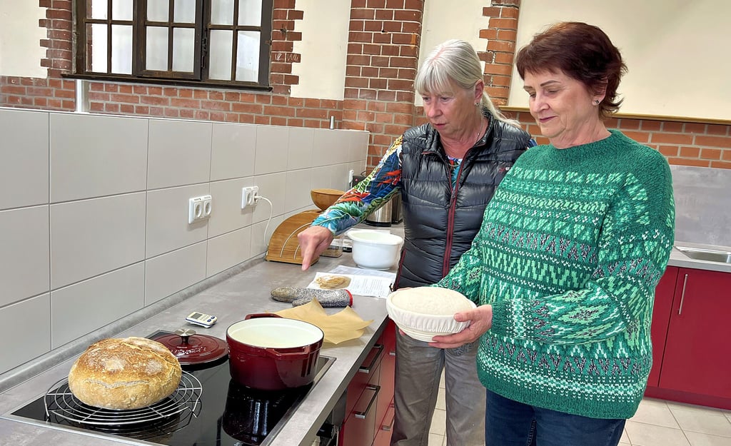 Heike Beckmann (rechts) nimmt unter Anleitung von Sandra Röpcke den Teigrohling im Gärkörbchen, um ihn fürs Backen in den gusseisernen Topf zu legen. Am Ende kommt ein rundes, knuspriges Brot, wie links im Bild, heraus. Die Bedingungen im Hauswirtschaftsbereich der Gemeinschaftsschule in Tangerhütte sind bestens für Kurse wie diesen geeignet.