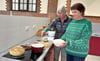 Heike Beckmann (rechts) nimmt unter Anleitung von Sandra Röpcke den Teigrohling im Gärkörbchen, um ihn fürs Backen in den gusseisernen Topf zu legen. Am Ende kommt ein rundes, knuspriges Brot, wie links im Bild, heraus. Die Bedingungen im Hauswirtschaftsbereich der Gemeinschaftsschule in Tangerhütte sind bestens für Kurse wie diesen geeignet.