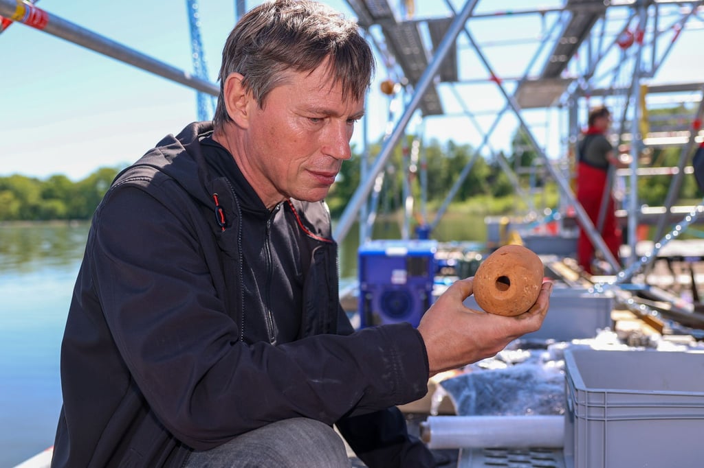 Der Unterwasserarchäologe Sven Thomas vom Landesamt für Denkmalpflege und Archäologie Sachsen-Anhalt zeigt einen auf dem Prahmboot entdeckten Netzbeschwerer.