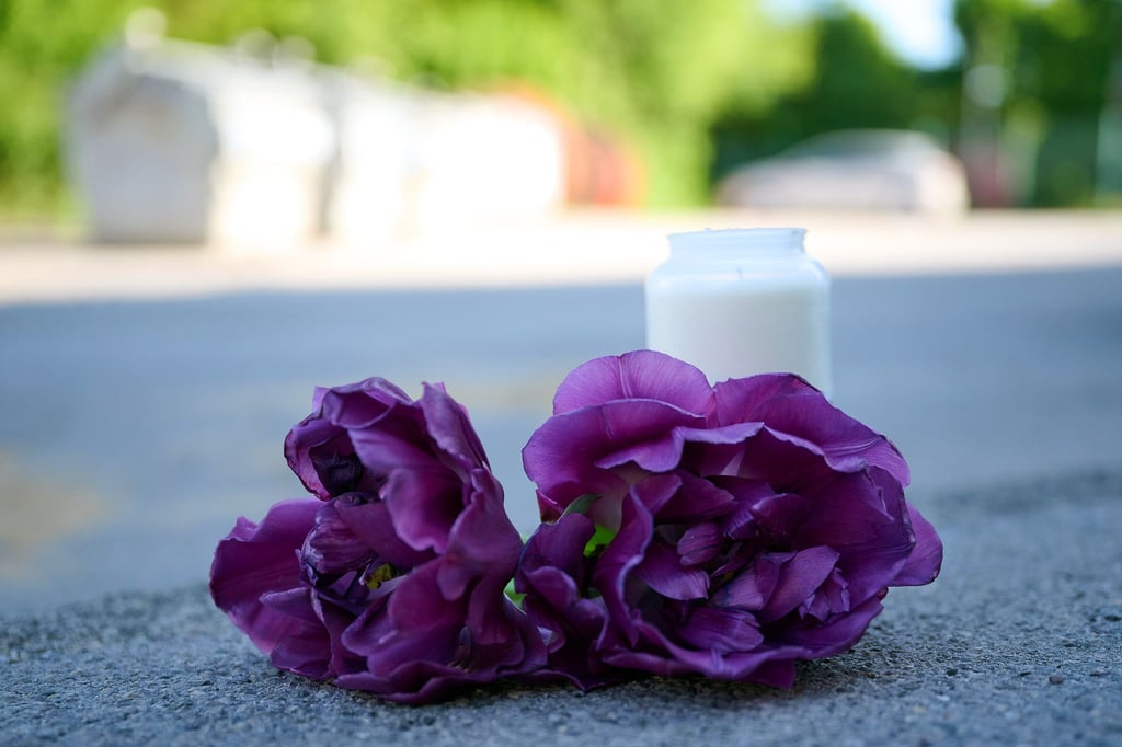 Blumen und eine Kerze liegen auf einem Schotterplatz vor dem Eingang zum Spielplatz, auf dem in der Nacht ein 17-Jähriger einen 14-Jährigen erstochen haben soll.