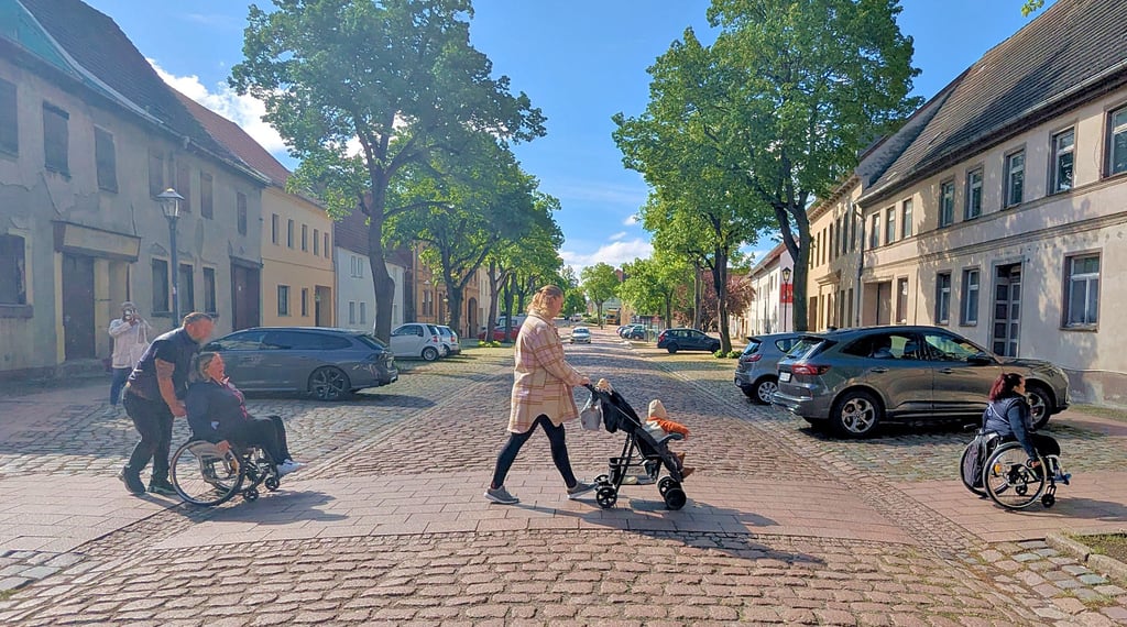 Vorne eine echte Rollstuhlfahrerin, eine Person mit Kinderwagen und eine Person, die testet, wie sich Rollstuhlfahren unter widrigen Straßenbedingungen anfühlt. Vor allem für die dritte im Bunde waren die Ablaufrinne am Straßenrand eine ziemliche Herausforderung.