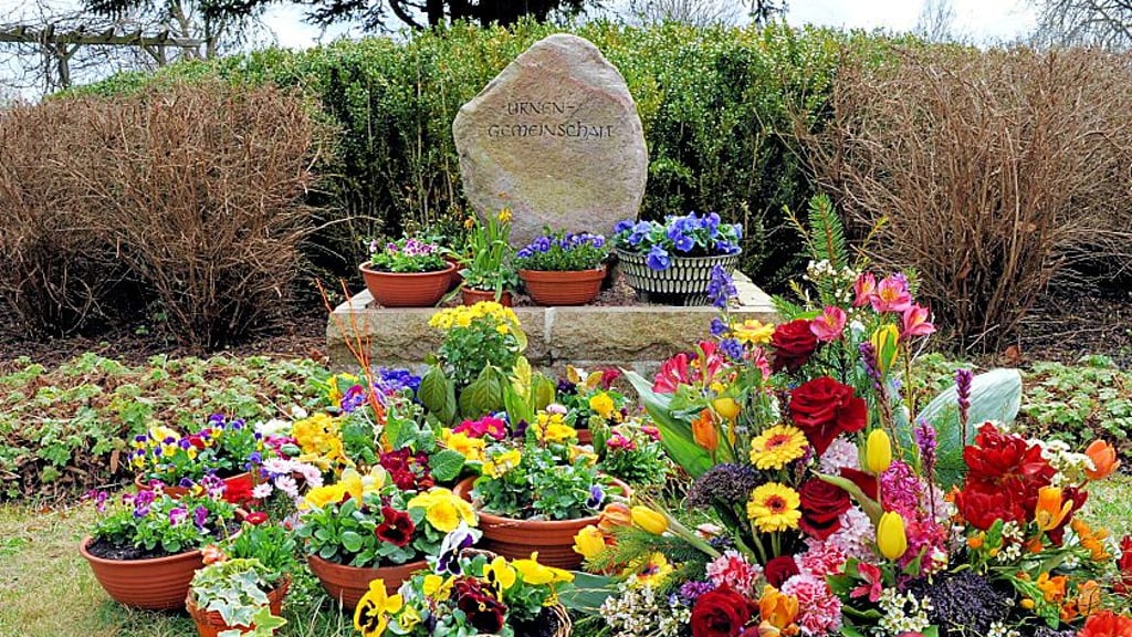 Blumen und Gebinde schmücken eine Urnengrabanlage.