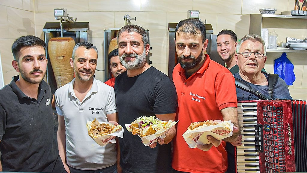 Yusuf Aydin (Mitte), Inhaber der Pizzeria „Zaza Jasmin“, sein Cousin Kasim Aydin (2.v.l.) und seine Mitarbeiter erleben einen Ansturm. Um die Wartezeit für die Kunden zu verschönern, spielt Wilfried Panksy (r.) auf seinem Akkordeon.
