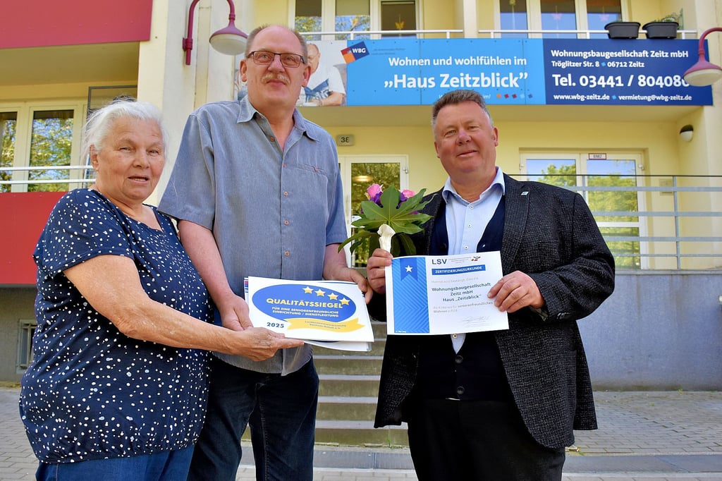 Erika Fischer und Andreas Huhnstock überreichten vor dem Haus Zeitzblick das Zertifikat „seniorenfreundlicher Service“ an Sven Weißbrodt von der Wohnungsbaugesellschaft Zeitz.