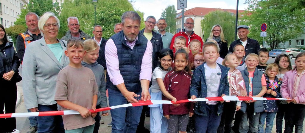 Bürgermeister Sven Hause (M.) zerschneidet hier das Band bei der offiziellen Eröffnung des neuen Calbenser Radweges im Beisein von Hortkindern der nahen Grundschule, einigen Stadträten und Mitarbeitern der beauftragten Baufirmen.