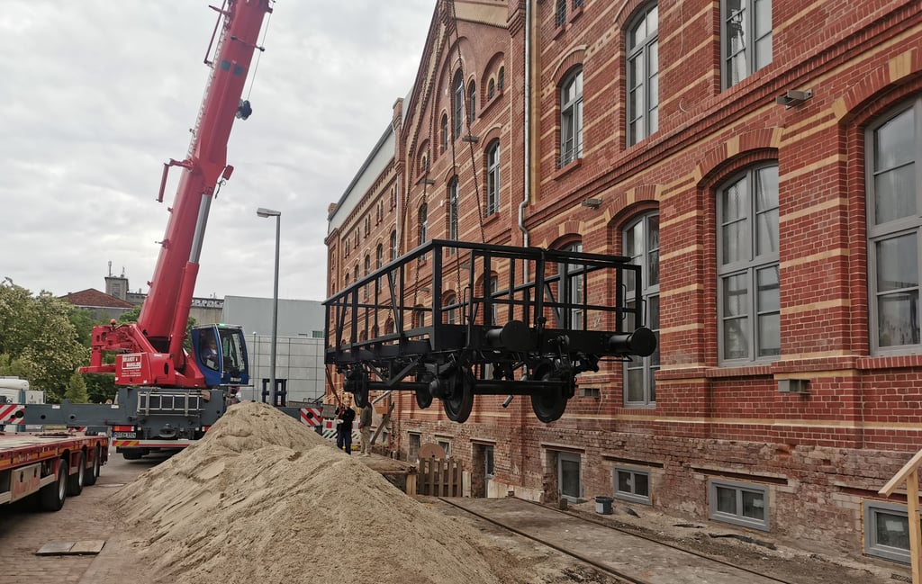 Ein Schwerlastkran hebt den ersten von vier Güterwagen auf das Gleis vor der ehemaligen Backwarenfabrik in Magdeburg.