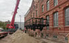 Ein Schwerlastkran hebt den ersten von vier Güterwagen auf das Gleis vor der ehemaligen Backwarenfabrik in Magdeburg.