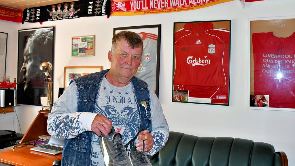 Udo Pütsch aus Schönhausen ist großer Fan des Liverpool FC. Hier die Fußballschuhe, die er 2013 auf dem Rasen des Anfield-Stadions getragen hat. Im Hintergrund Trikots und Schals und ein Porträt von John Lennon.