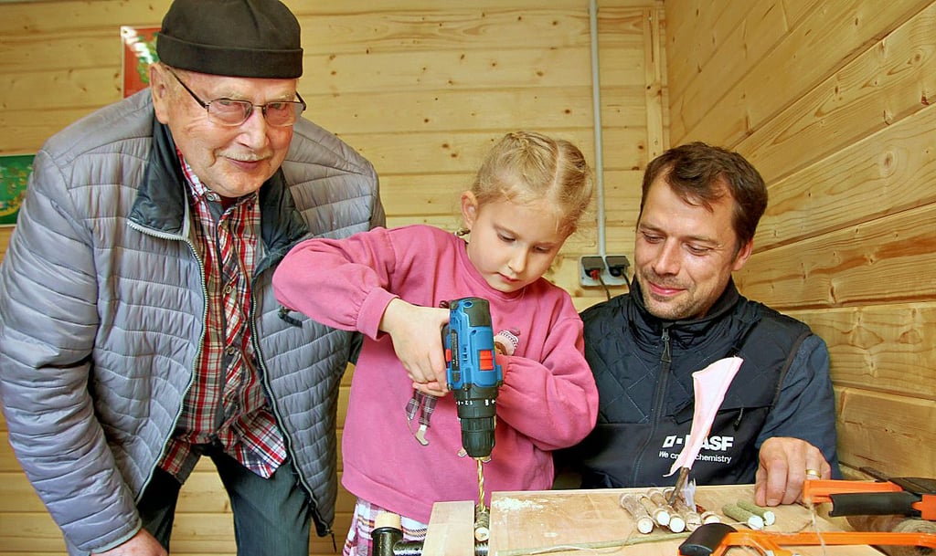 Bernd Gaedecke (li.) und Enkelin Mara bauen in der Holzwerkstatt mit Hilfe von Heiko Brandt ein Floß.