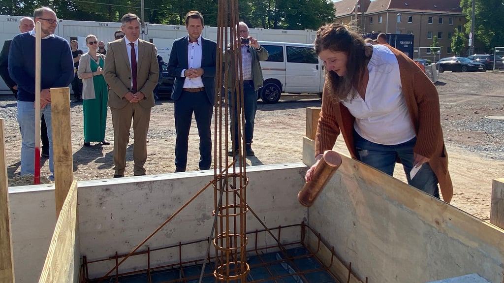 Stefanie Zacharias-Srocke, Projektleiterin bei Cureus, packt die Zeitkapsel für die Grundsteinlegung der neuen Seniorenwohnanlage am Goldbach in Halberstadt in die Metallbewährung. Compassio-Geschäftsführer Johannes Knake, Landrat Thomas Balcerowski und Oberbürgermeister Daniel Szarata (von links) schauen zu.