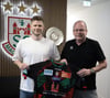 Sebastian Barthold zeigt zusammen mit SCM-Geschäftsführer Marc-Henrik Schmedt, für welchen Verein er nächste Saison spielen wird.
