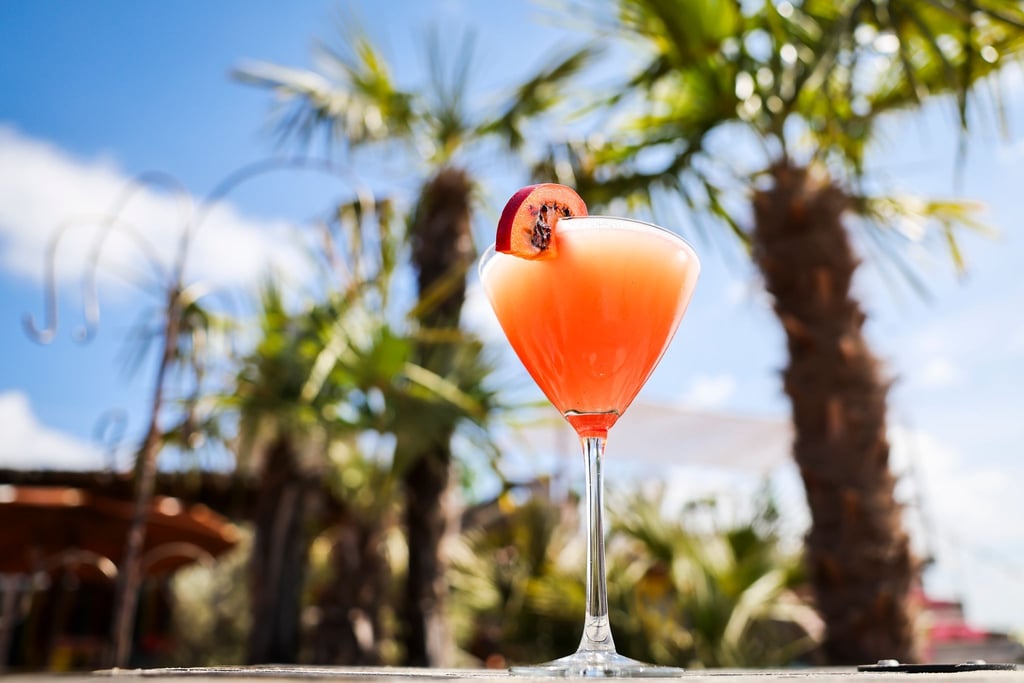Ein Passionsfrucht Martini (auch Pornstar Martini oder Maverick Martini genannt) steht unter Palmen auf einem Tisch in einer Strandbar.