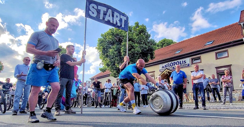 Robert Kutz nimmt in Hoym mit dem Fass die 5.570 Meter nach Badeborn in Angriff. Viele Radfahrer und links Schiri Maik Lehrmann, begleiten ihn.