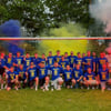 Meister unter sich – Arm in Arm, voller Stolz und mit breitem Grinsen: Spieler der ersten und zweiten Mannschaft feiern den gemeinsamen Aufstieg. Im Hintergrund leuchten blau-gelbe Bengalos – ein emotionaler Moment in Vereinsfarben.