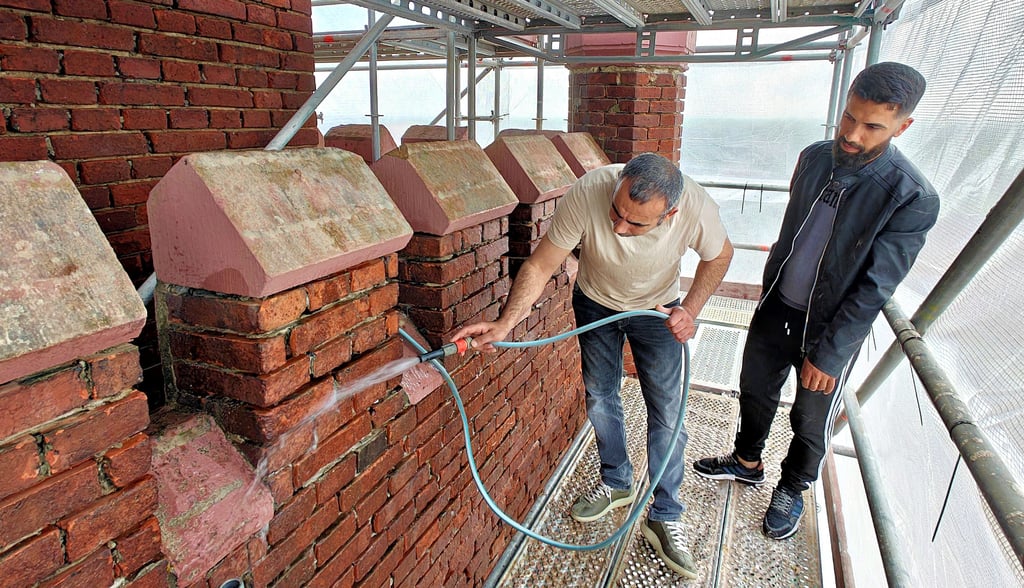 Nihad Bitmez (l.) und Baki Ucucu spülen jede einzelne ausgekratzte Fuge des Turms vor der Neuverfugung aus.