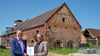 Kulturstaatssekretär Sebastian Putz übergibt vor der Scheune den Förderbescheid an den Abteilungsleiter Baudenkmalpflege Robert Hartmann.