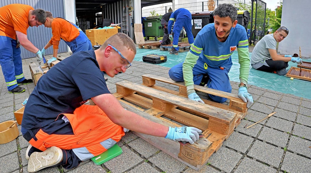 Azubi Muhamad Alasakr (2. von rechts) leitet einen Schüler beim Schleifen von Paletten an.