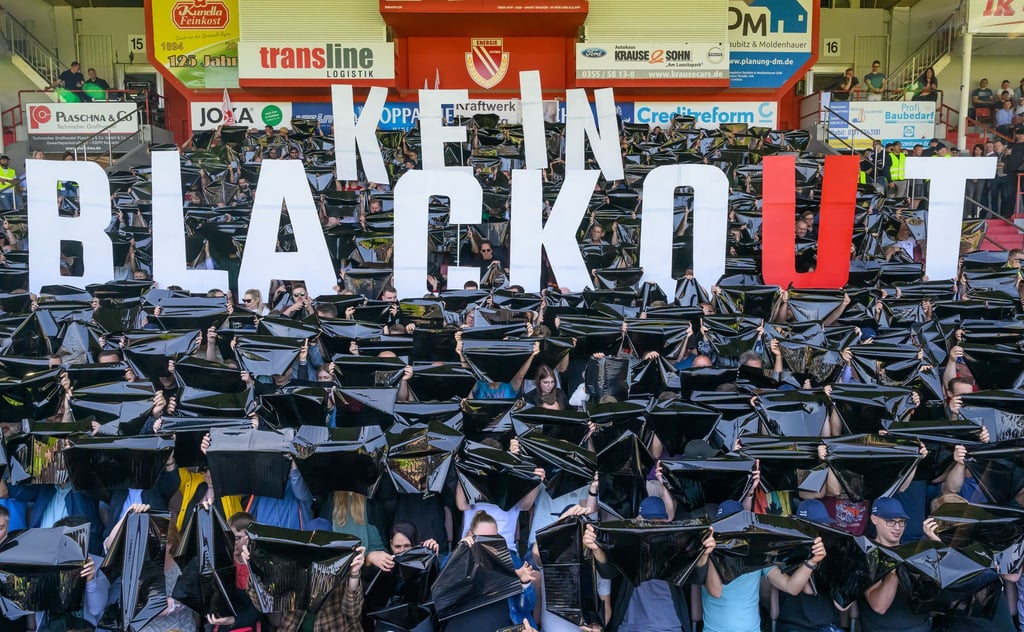 Leag-Beschäftigte halten bei einer Betriebsversammlung im Fußballstadion in Cottbus den Spruch „Kein Blackout“ hoch.