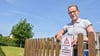 Annett Pätz, Mitarbeiterin des Ordnungsamtes der Verbandsgemeinde Flechtingen, bringt Warnschilder am Zaun des Spielplatzes an der Straße  Langer Steig in Calvörde an. Im Hintergrund ist eine befallene Eiche zu sehen.
