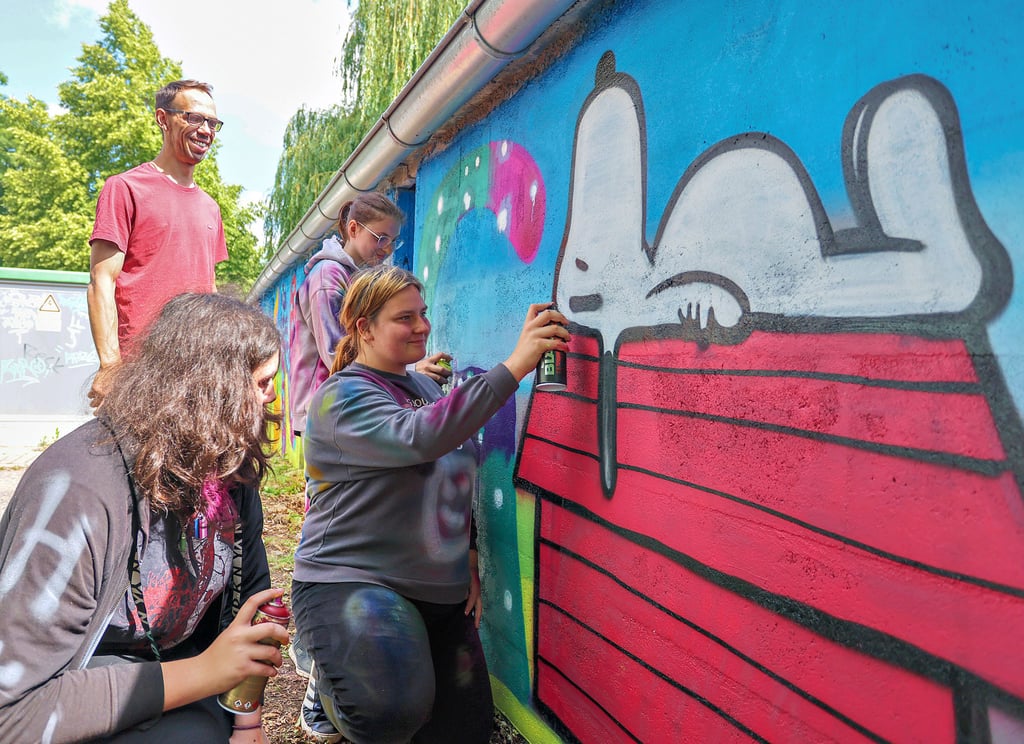 Eine der Figuren, die die Petalozzischülerinnen und -schüler bei ihrer Graffitiaktion auf der zuvor grauen Wand aufbrachten, war Hund „Snoopy“. Projektleiter Martin Bölke schaut den Schülerinnen Chayenne Grünewald, Aileen Rudolph und Hannah Pentzold (v.l.) beim Sprühen zu.