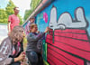 Eine der Figuren, die die  Petalozzischülerinnen und -schüler bei ihrer Graffitiaktion auf der zuvor grauen Wand aufbrachten, war Hund „Snoopy“.  Projektleiter Martin Bölke schaut den  Schülerinnen Chayenne Grünewald, Aileen Rudolph und Hannah Pentzold  (v.l.) beim Sprühen zu. 