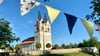 Eine bunte Wimpelkette zieht sich durch Minsleben zum 1.025-jährigen Jubiläum des Dorfes bei Wernigerode - auch an der Kirche St. Margareten entlang.