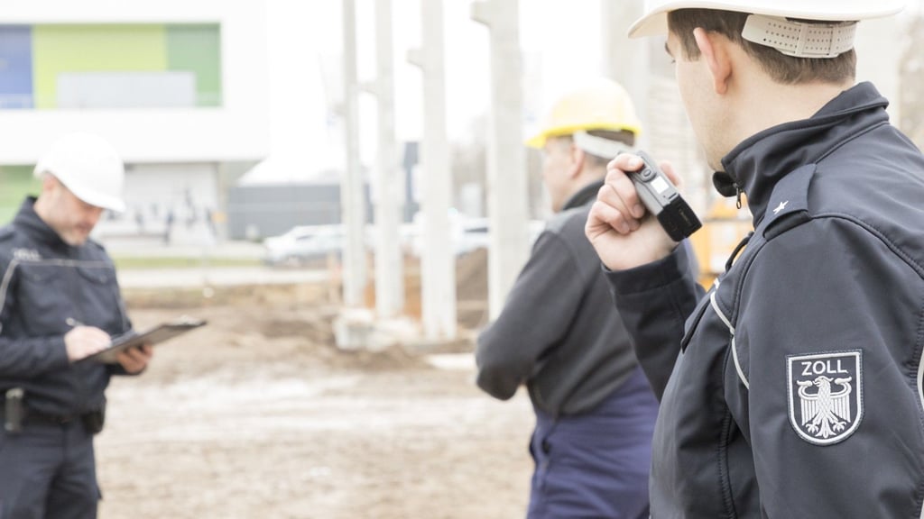 Zoll-Beamten kontrollieren Arbeiter auf einer Baustelle.