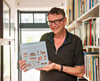 Der Grafikdesigner Ad van der Kowe in seinem Haus mit dem zweiten Band seines Projekts „1.000 Fassaden“ anlässlich des kommenden Stadtjubiläums. Am Freitag wird eine weitere Ausstellung in der Kunsthalle eröffnet.  