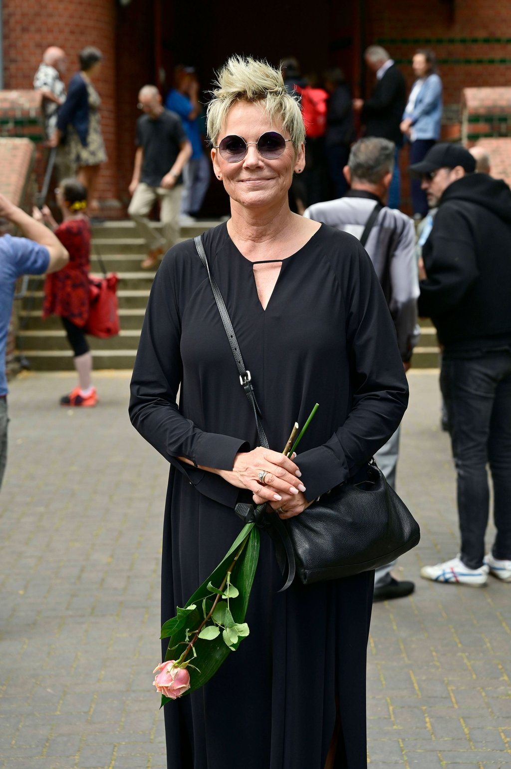 In einem schwarzen Kleid und mit dunkler Sonnenbrille auf bringt sie für die verstorbene Urte Blankenstein eine Rose mit.